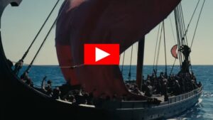 Scena del film Odissea di Christopher Nolan con una nave in mare e il simbolo di riproduzione